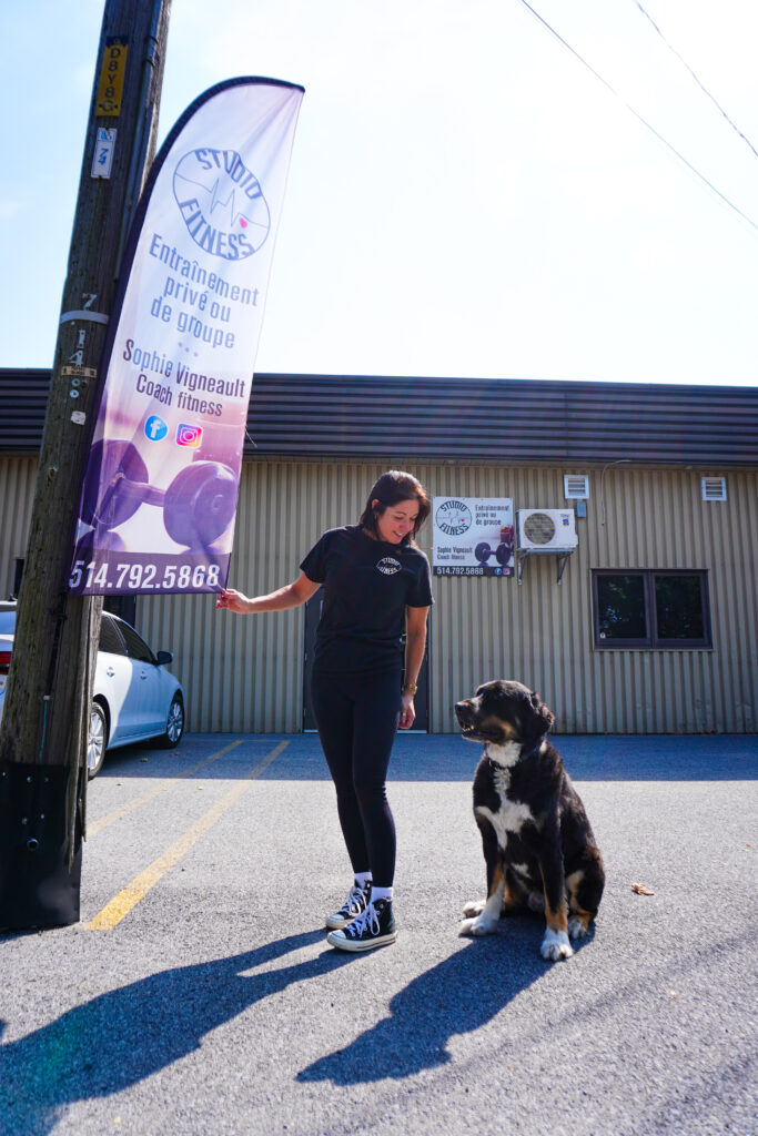 Coach Sophie devant le Studio Fitness Beauharnois, accompagnée de son chien, sous l’enseigne du gym.